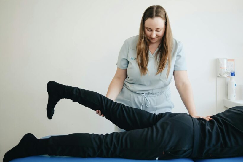 A physiotherapist helps a patient stretch their leg during a therapy session in Vilnius clinic.